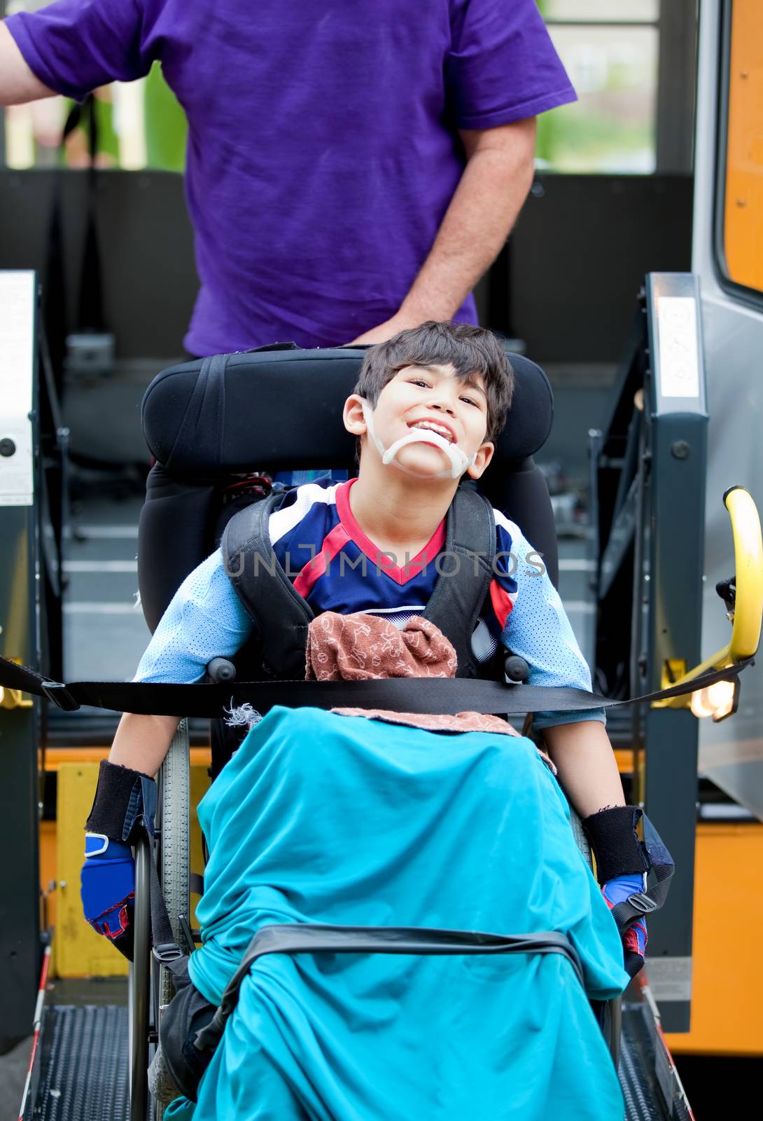 Happy disabled seven year old boy being transported on handicap school bus lift