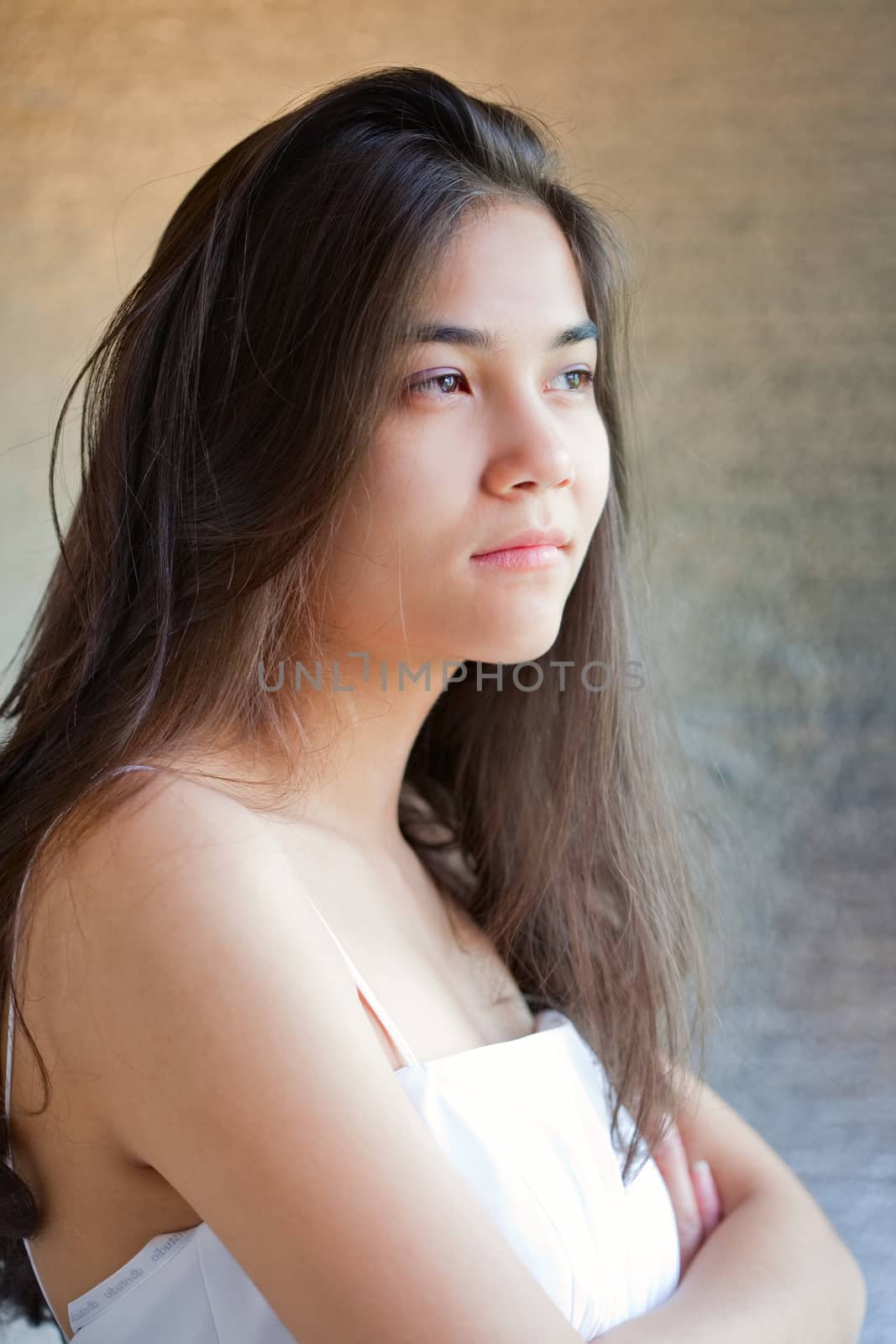 Biracial teen girl in white gown, arms crossed looking off to side