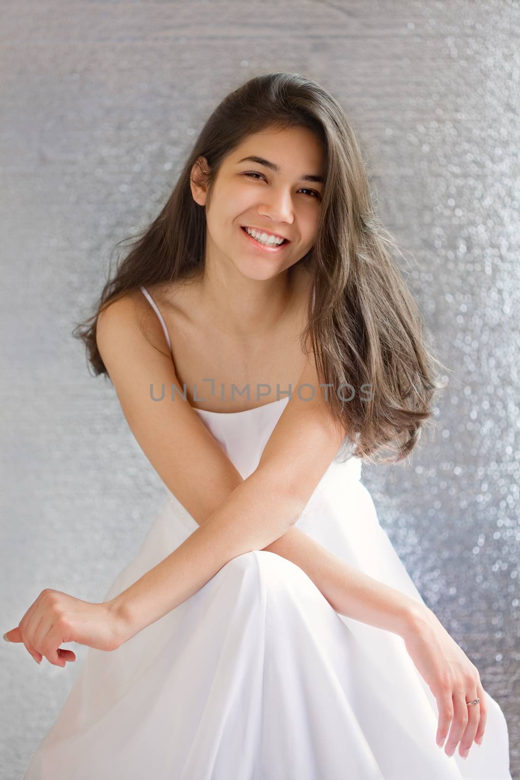 Beautiful biracial teen girl in white dress, sitting arms crossed at knees