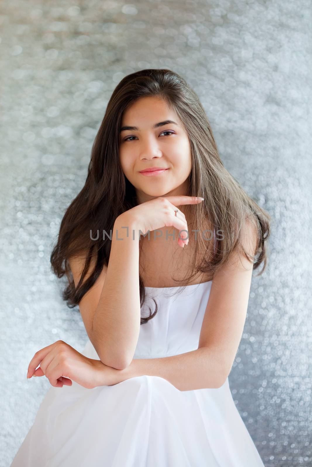 Beautiful biracial teen girl in white dress sitting, thinking towards camera