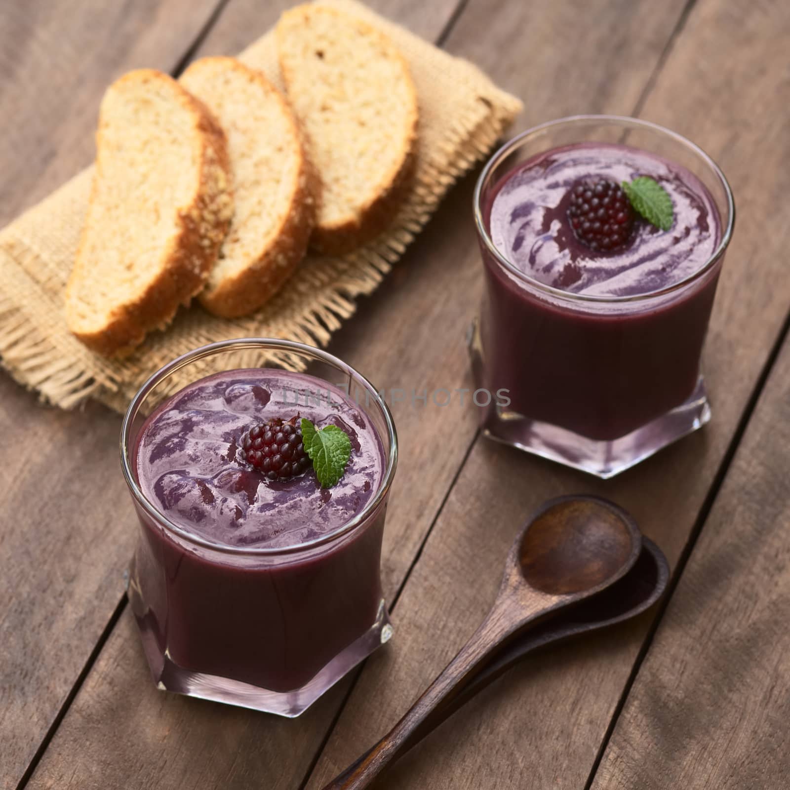 Ecuadorian traditional thick drink called Colada Morada, prepared by cooking purple corn flour and different fruits (for example strawberry, pineapple, naranjilla, grape, babaco, blackberry, etc) and seasoned with panela (cane sugar), cinnamon, allspice and cloves; accompanied by bread (Selective Focus, Focus on the blackberry on the first drink)