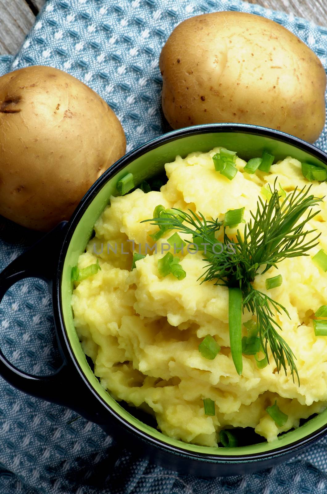 Delicious Homemade Mashed Potato with Dill and Spring Onion in Dark Blue Casserole closeup on Blue Napkin. Top View