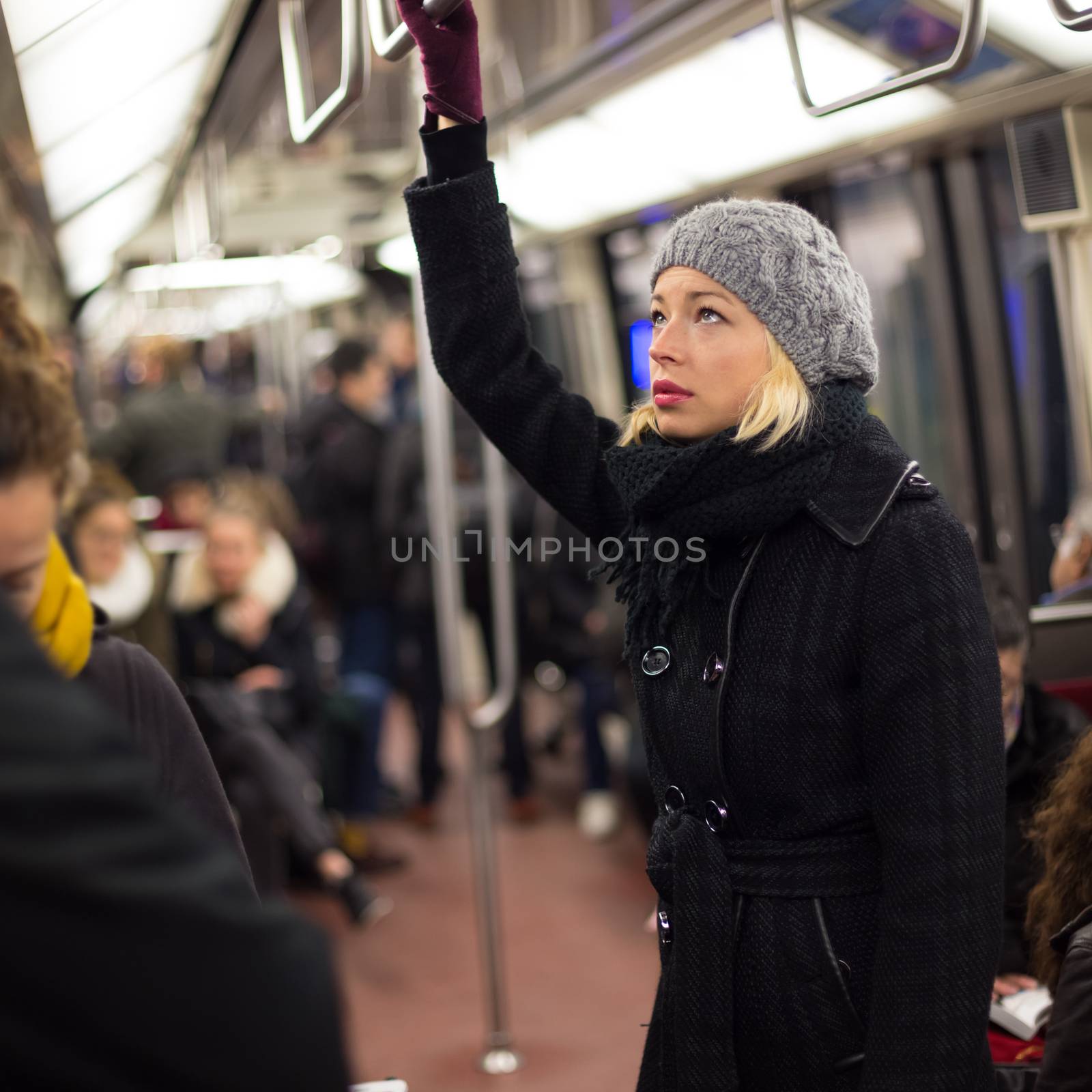 Beautiful blonde caucasian lady wearing winter coat traveling by metro in rush hour. Public transport.