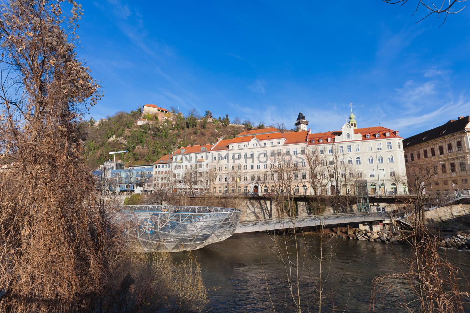 Graz, Austria - January 16, 2011: Island on Mur river connected by a modern steel and glass bridge, Styria, Graz, Austria