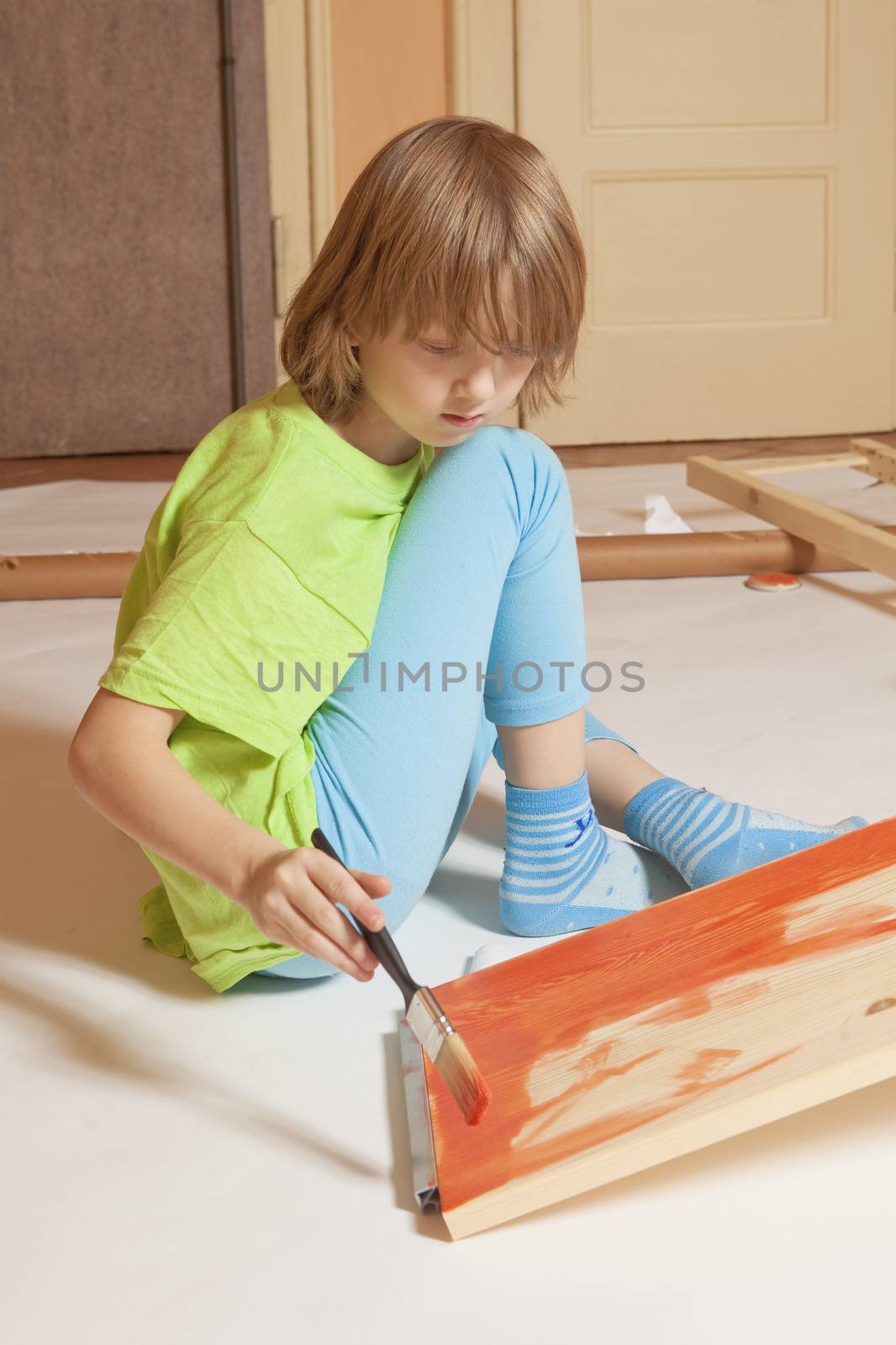 Boy with Blond Hair Painting a Board with Red Color