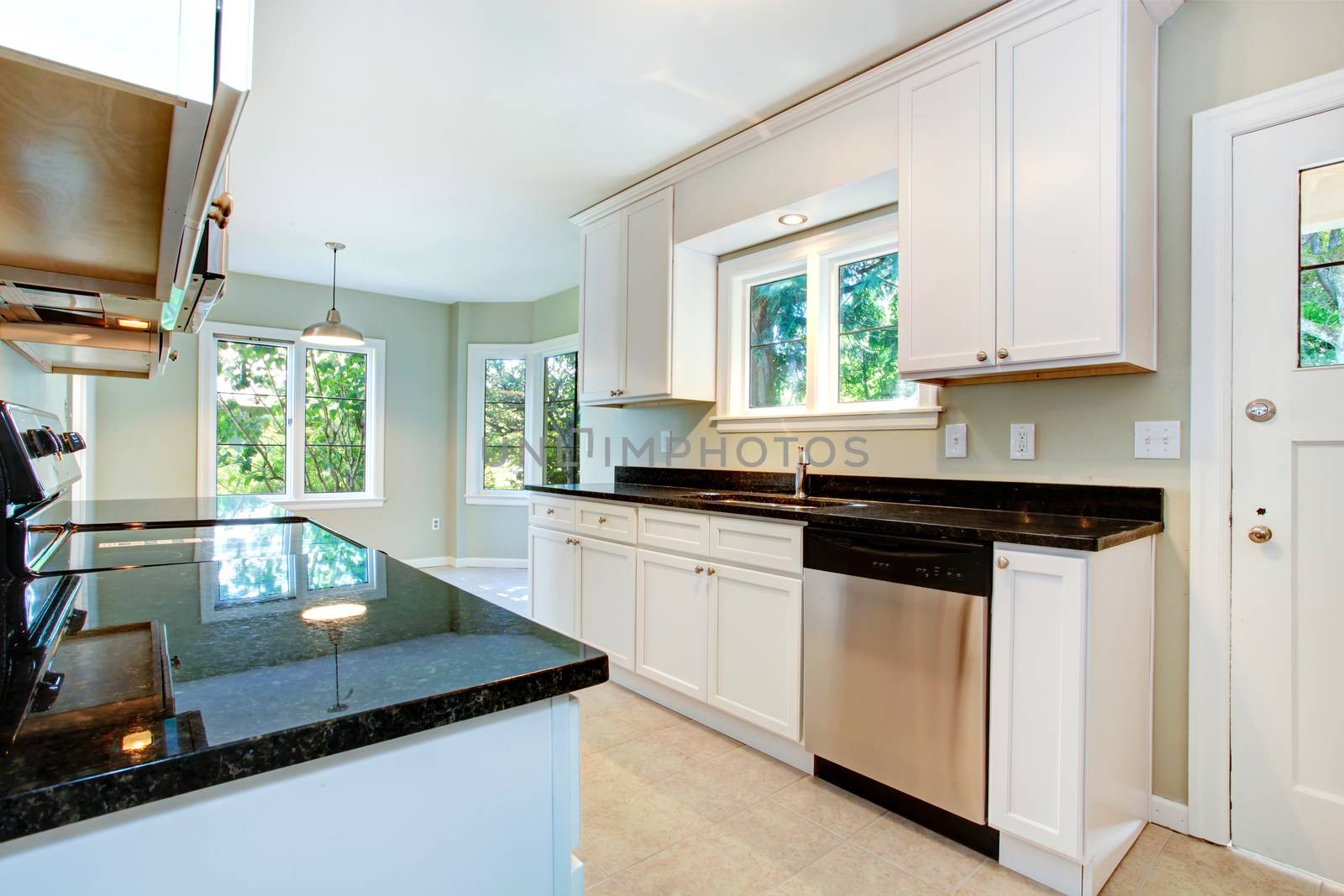 White ktichen cabinets with black granite tops and steel dish washer. Kitchen with empty dining area