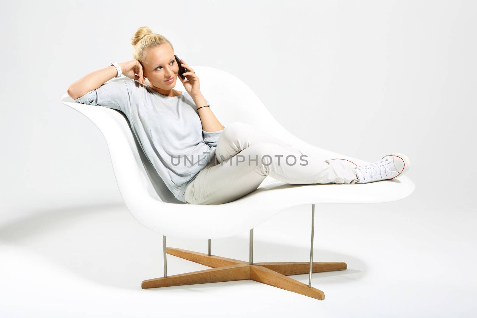 Blonde talking on mobile phone while sitting on a stylish white chair