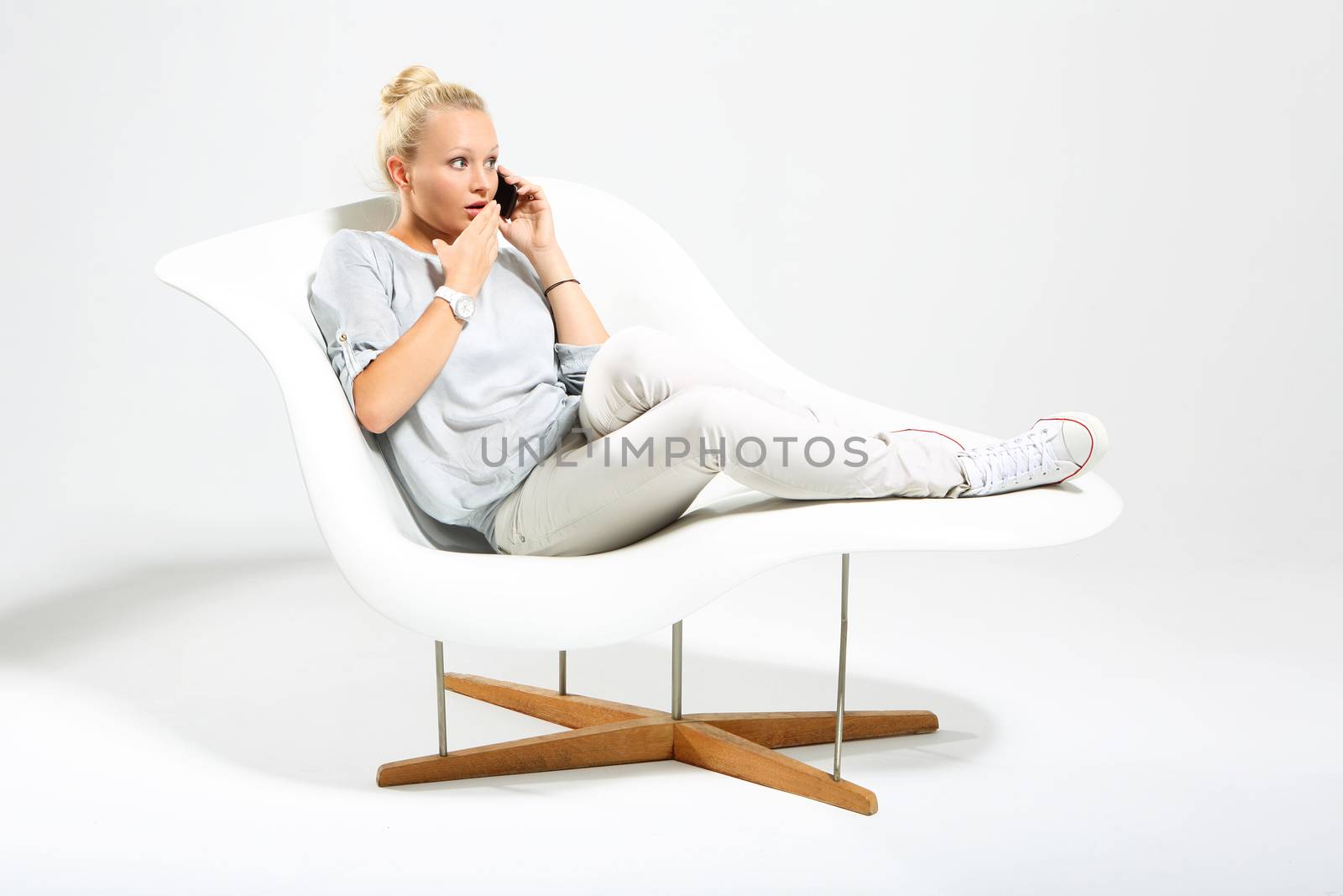 Blonde talking on mobile phone while sitting on a stylish white chair by robert_przybysz