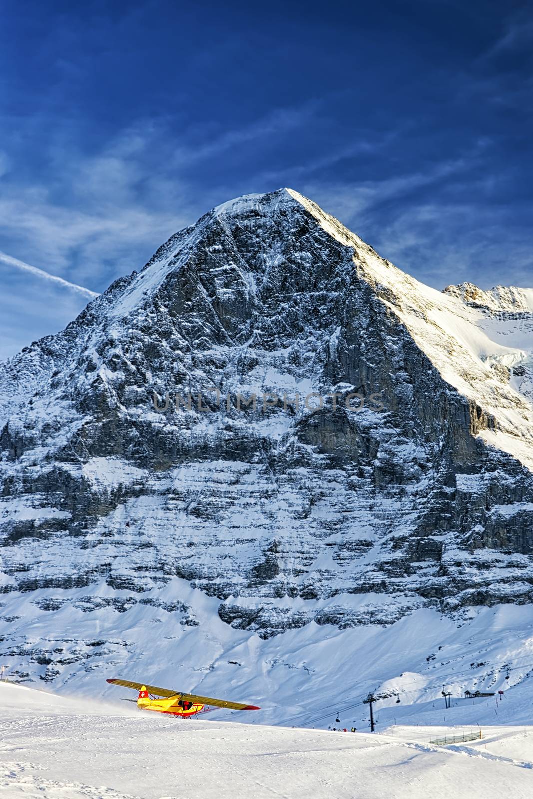 Yellow airplane taking off from alpine resort in swiss alps in winter