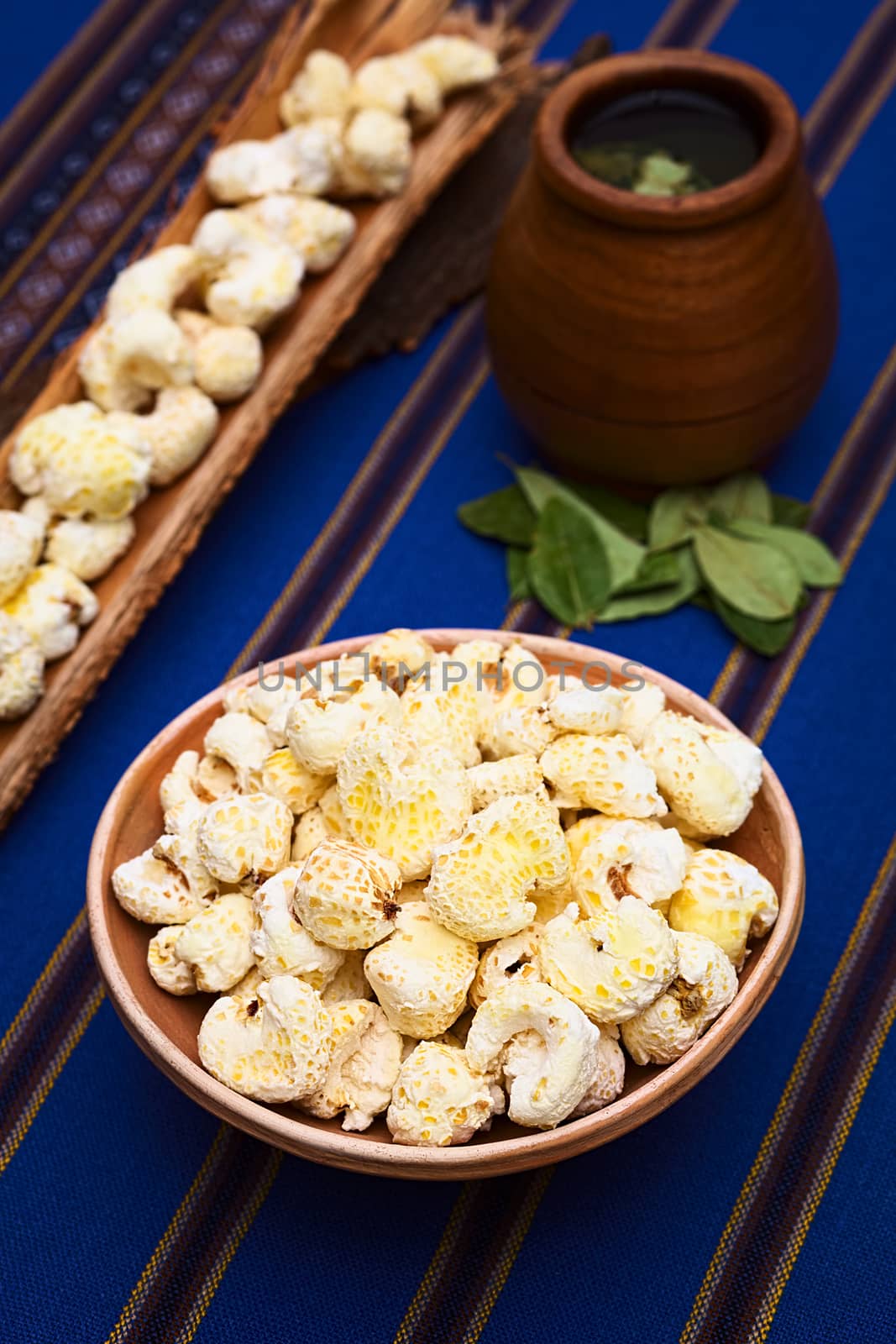 Sweetened popped white corn called Pasancalla eaten as snack in Bolivia served in a clay bowl with coca tea in the back, photographed with natural light (Selective Focus, Focus on the first half of the snack) 
   