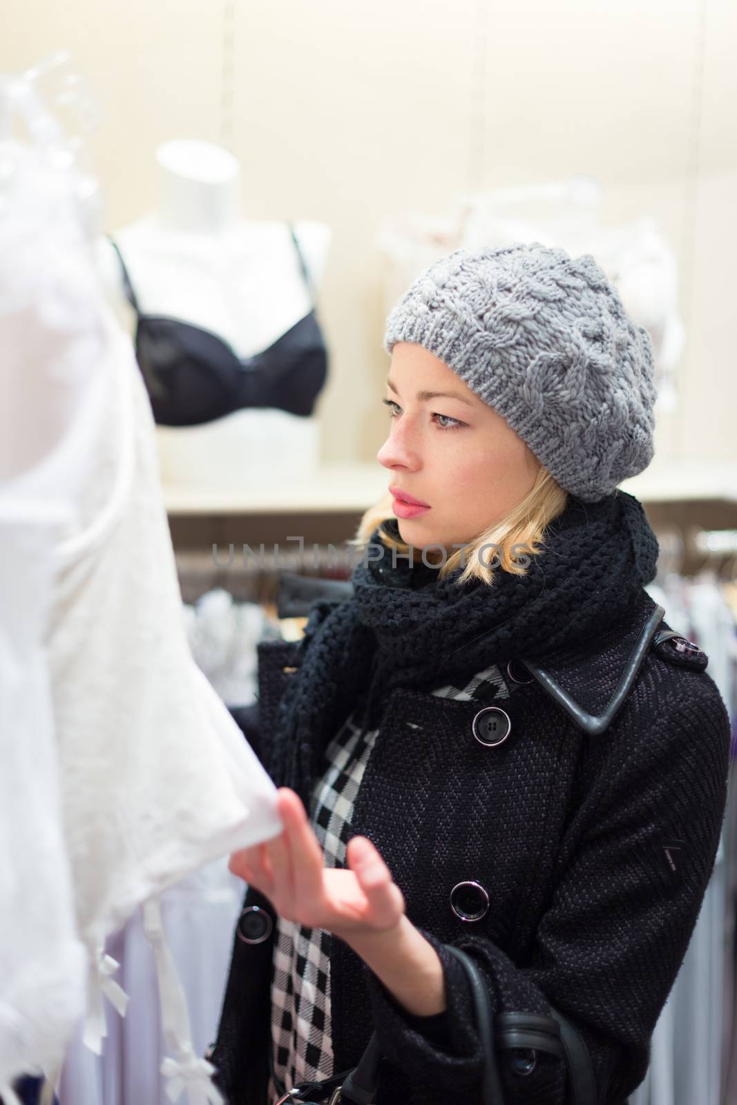 Woman shopping lingerie . Shopper looking and choosing clothing indoors in store. Beautiful blonde caucasian female model wearing winter coat and fashionable knitted cap.