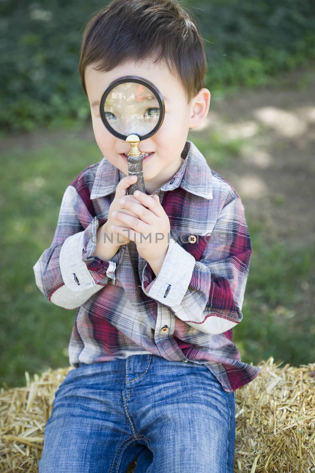 Cute Young Mixed Race Boy Looking Through Magnifying Glass Outside on Hay Bale.