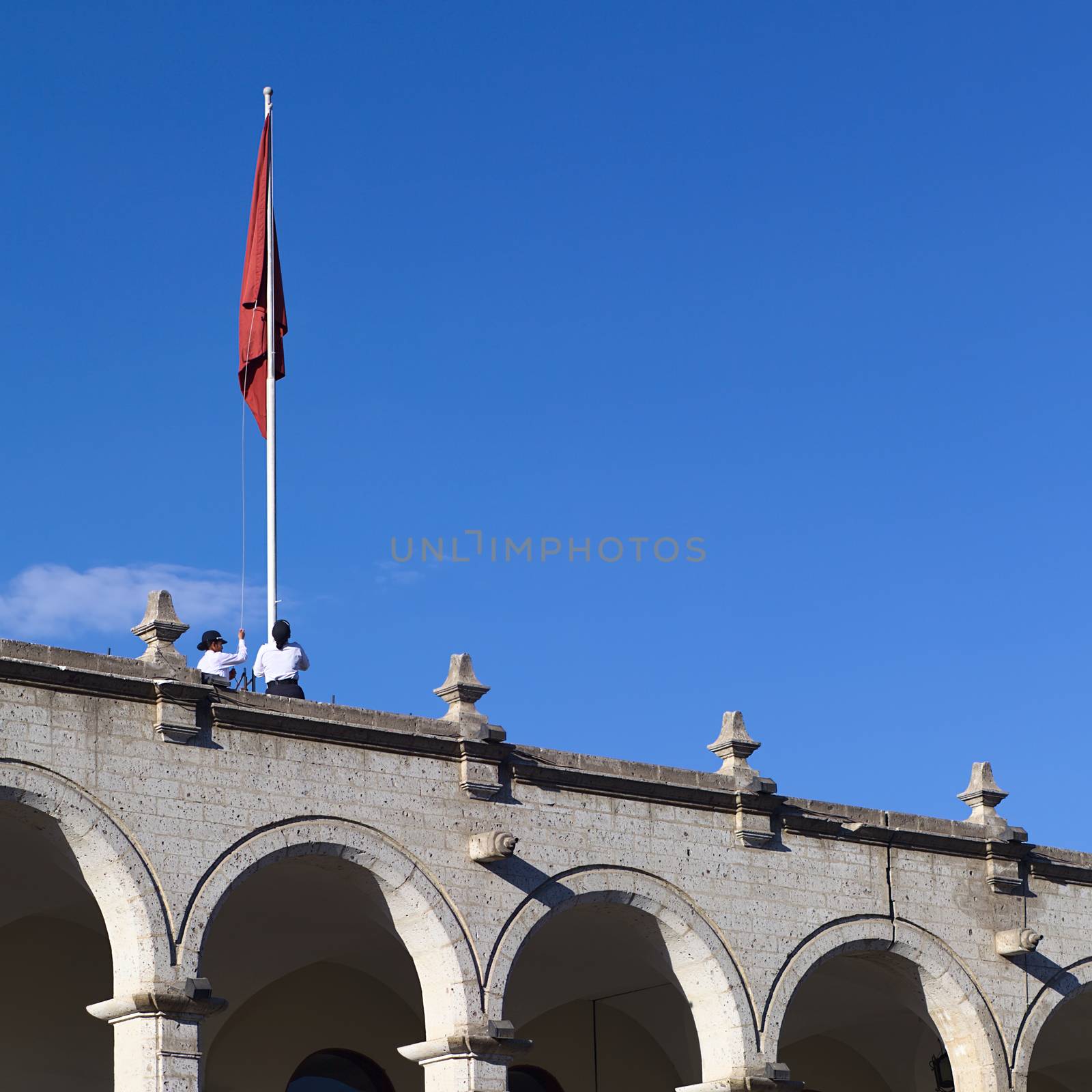 AREQUIPA, PERU - OCTOBER 8, 2014: Unidentified women pulling up the flag of Arequipa onto a flagpole on top of the city hall along Portal de la Municipalidad at the Plaza de Armas (main square) in the morning on October 8, 2014 in Arequipa, Peru