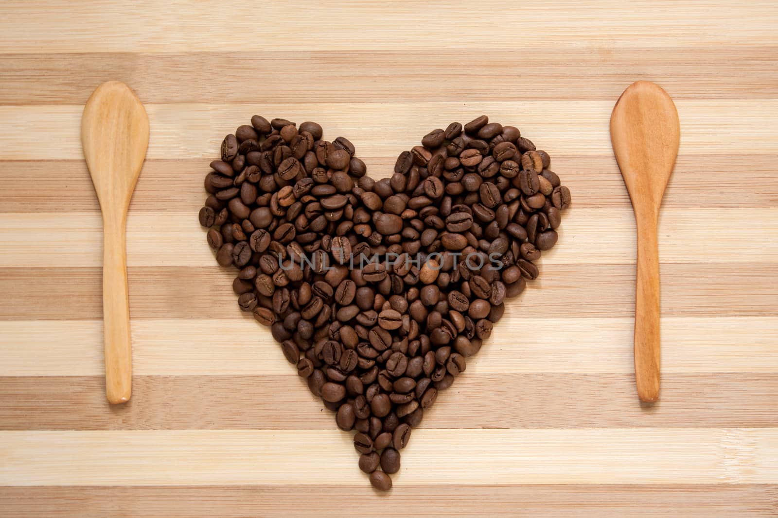 Heart of coffee beans with wooden spoons on wooden board.