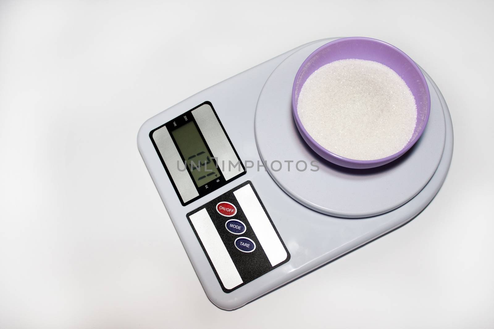 Bowl with sugar on the digital kitchen scale on the white background.