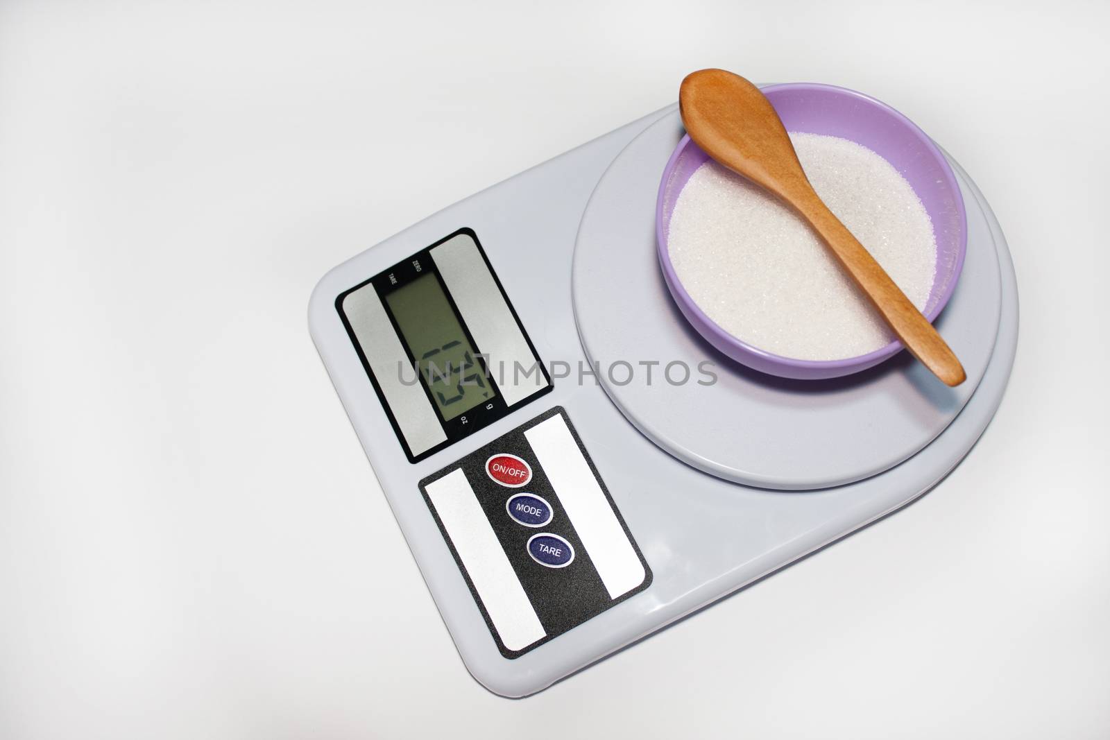 Bowl with sugar and wooden spoon on the digital kitchen scale on the white background.