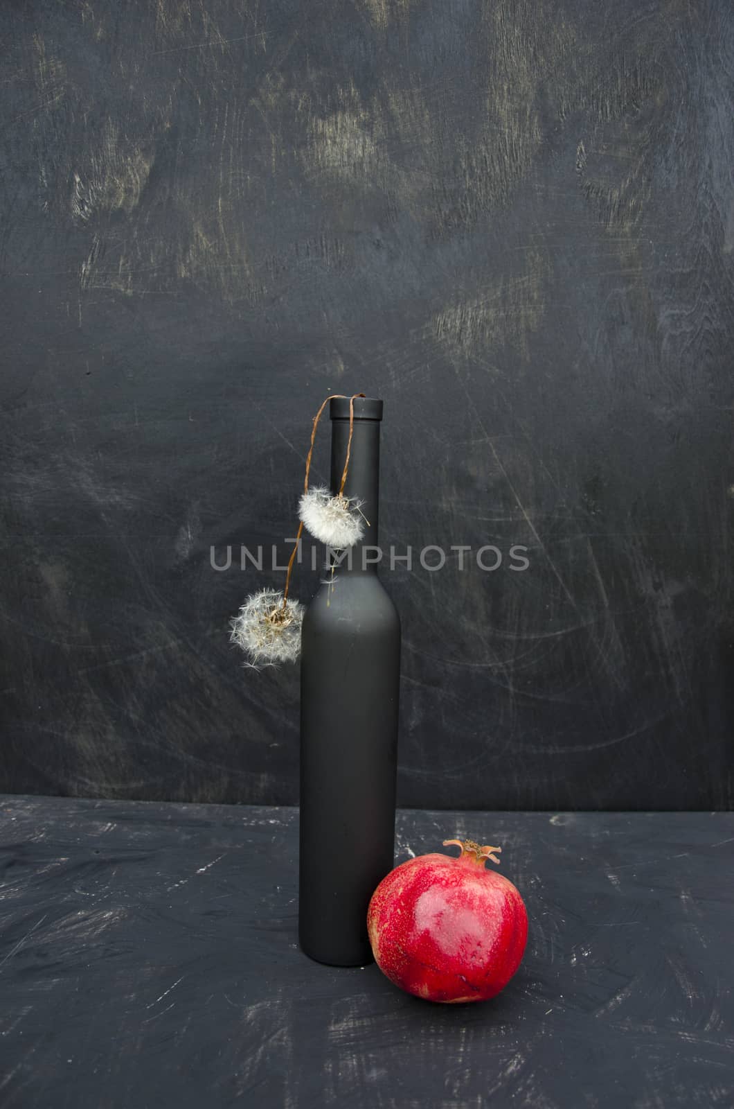 still life with black bottle, red pomegranate and dandelion seeds