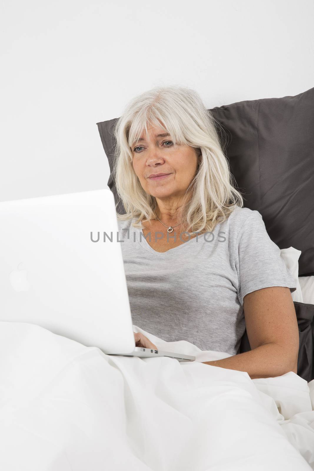 Mid Age woman with a laptop in bed by gemenacom