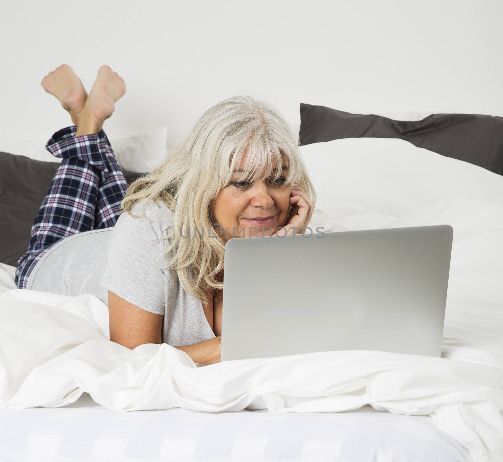 Mid age woman with a laptop lying down in bed