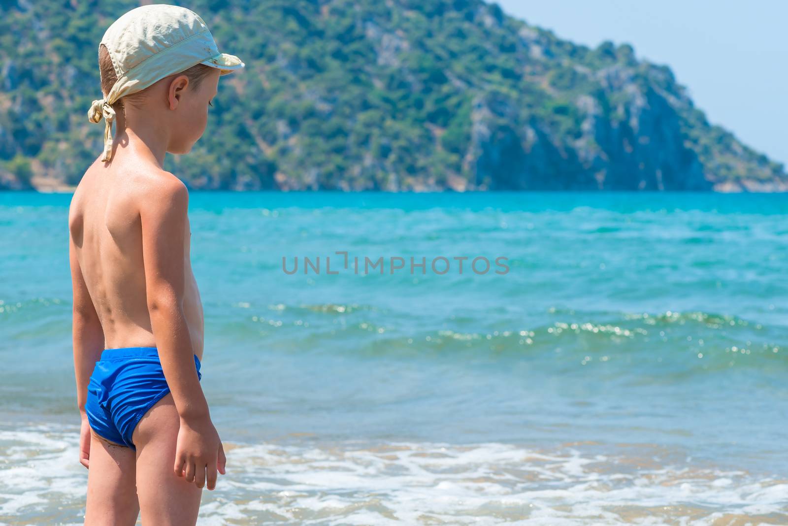 5 years old boy in swimming trunks is looking at waves by kosmsos111