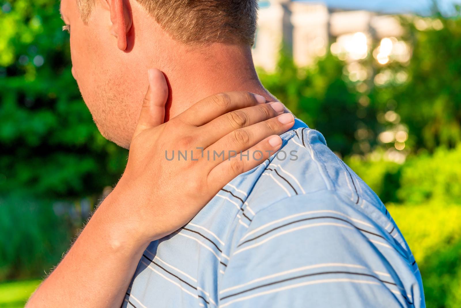 male massaging sore shoulder outdoors