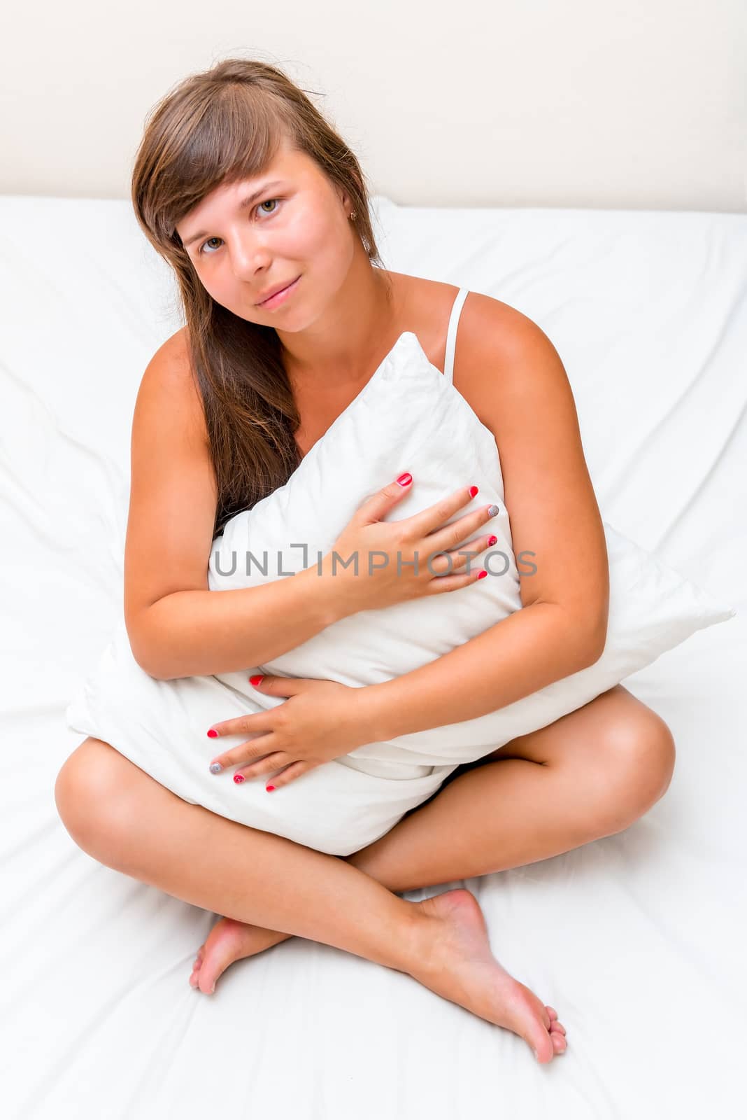 a charming young girl hugging a pillow in bed