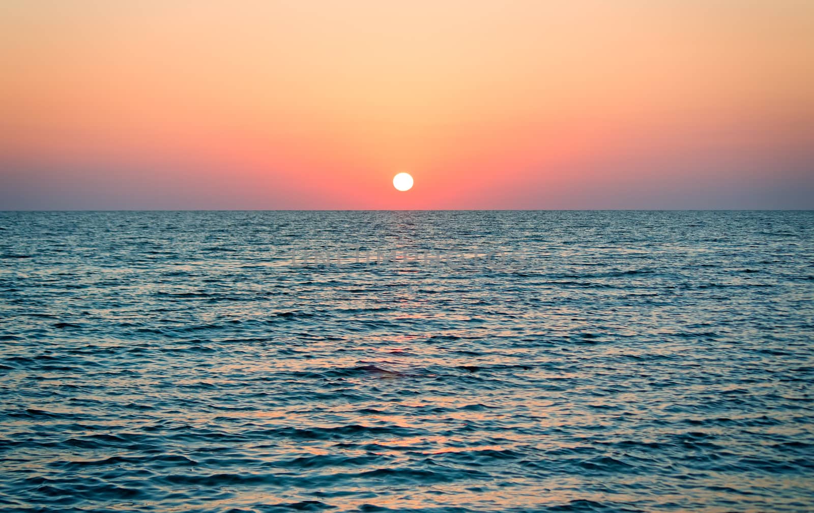 Seascape: the calm blue sea and the sun, leaning toward the horizon.