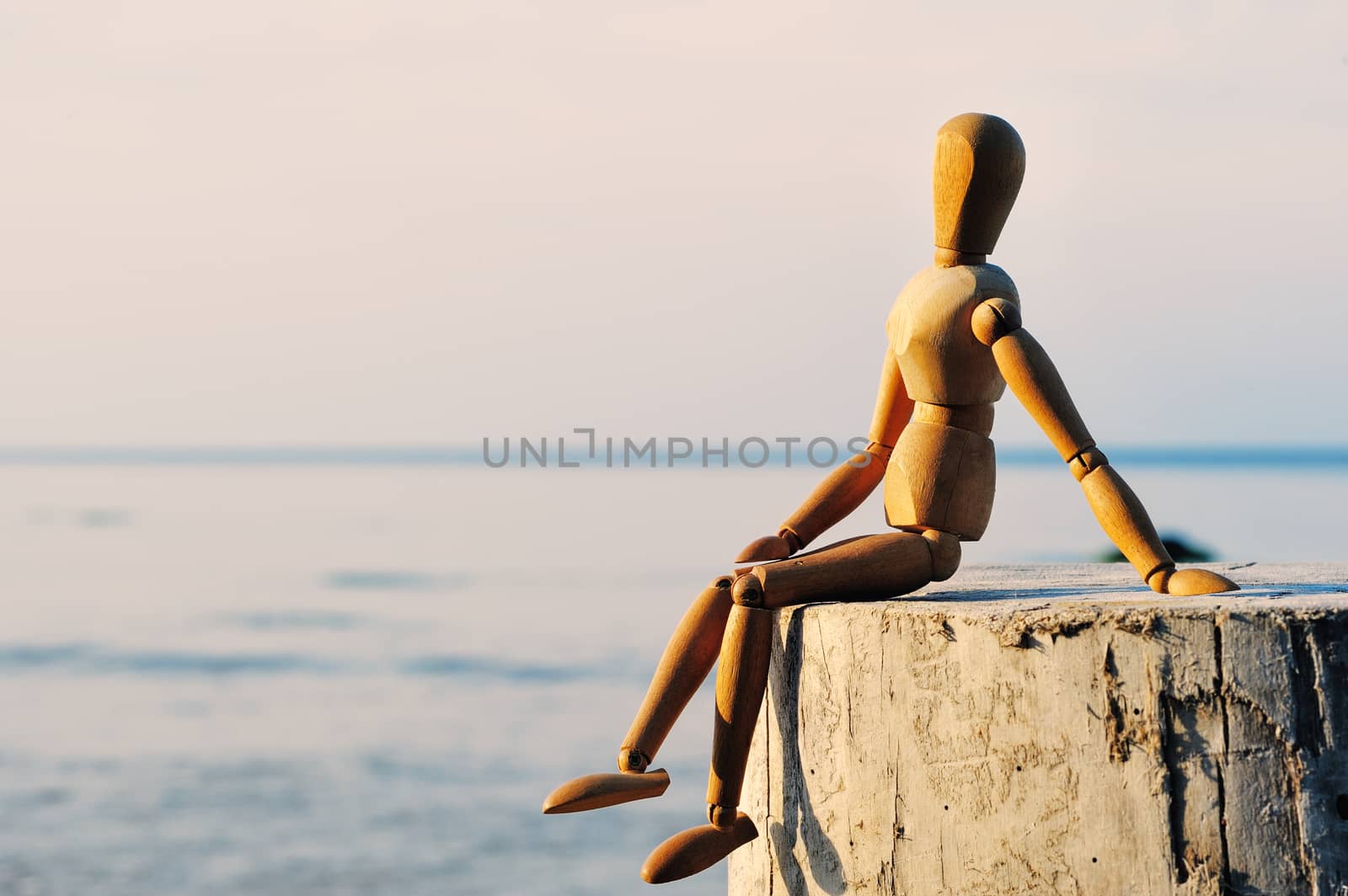 Wooden female figure sitting on the stump at the sea