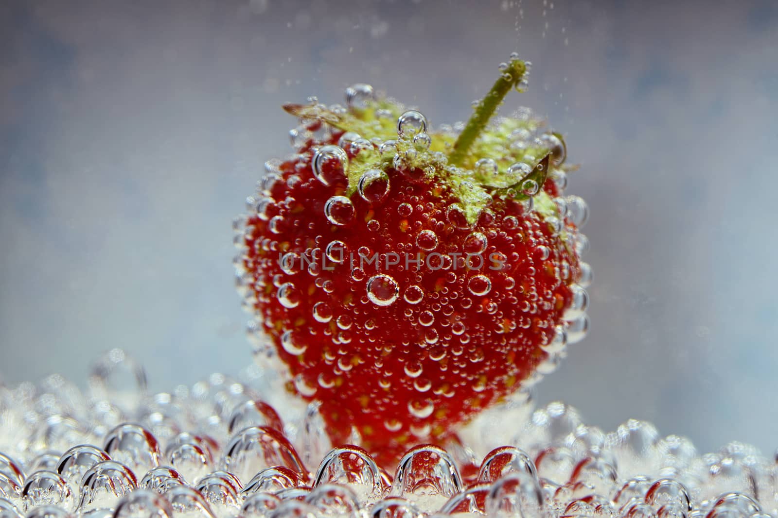 Photo of a strawberry with bubbles - underwater, on a blue background. Creative food photography.