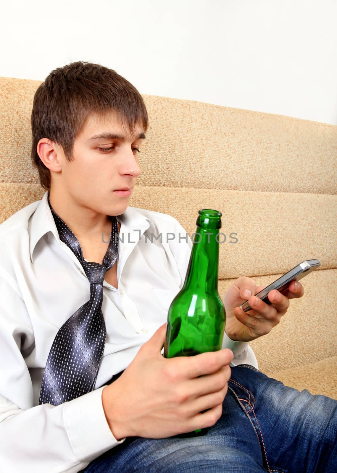 Teenager with Bottle of the Beer and Cellphone on the Sofa at the Home