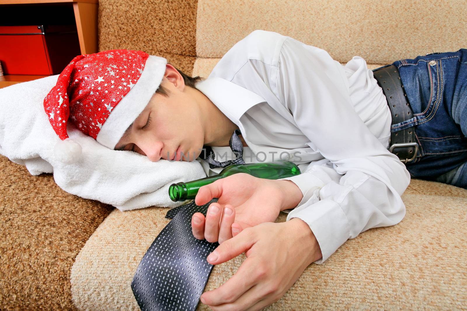 Drunken Teenager sleeping in Santa Hat and Bottle of the Beer on the Sofa