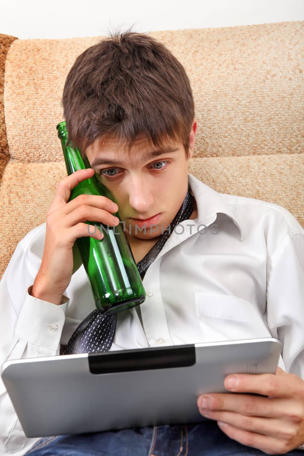 Stressed and Tired Teenager with a Beer and Tablet Computer on the Sofa at the Home