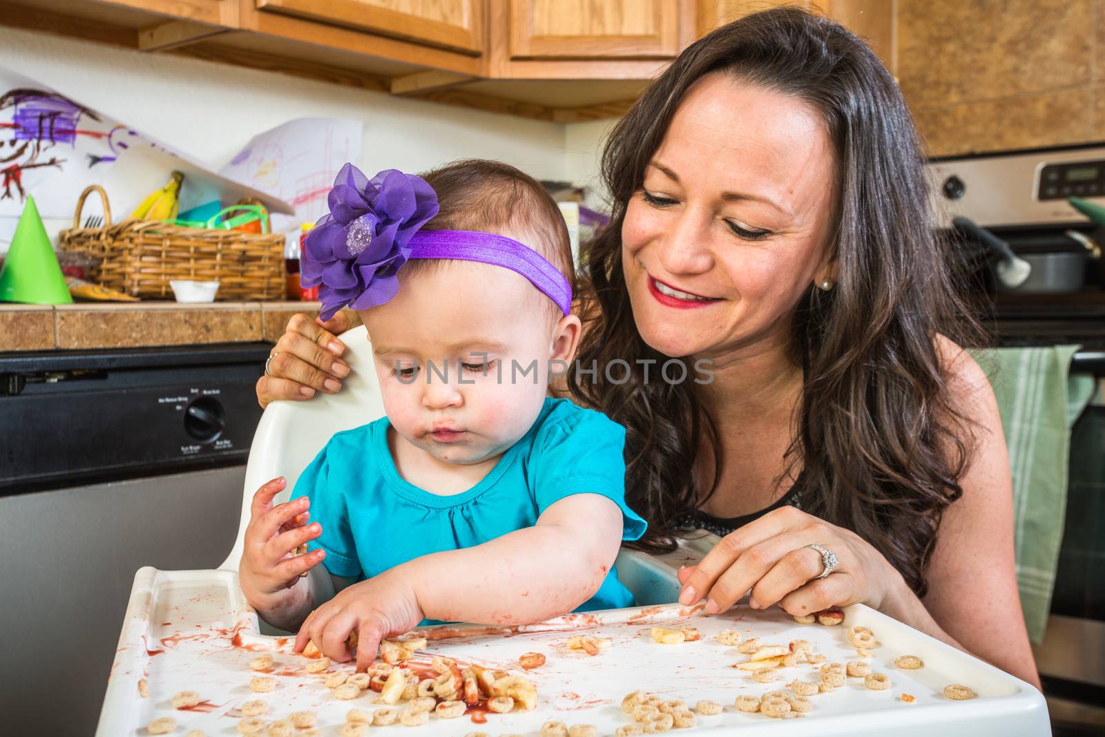 Mother in messy kitchen smiles as baby eats