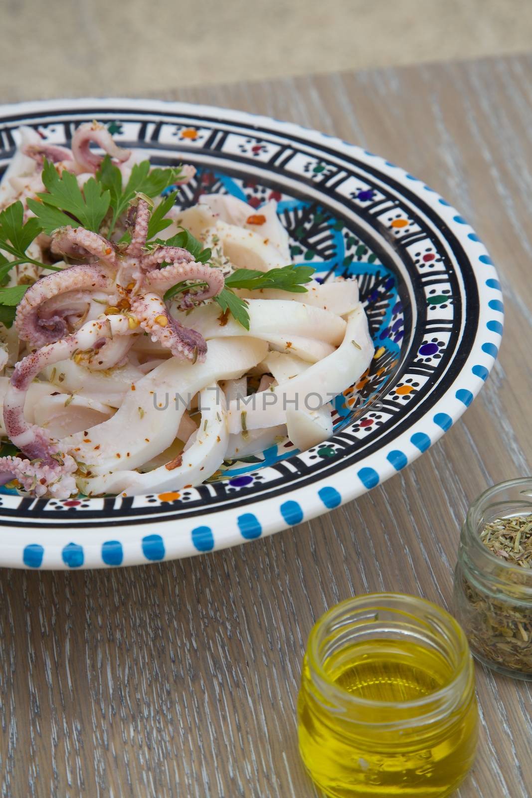 Marinated squid salad with fresh parsley in the traditional Tunisian plate. Oregano, olive oil and squeezed lemon in the background