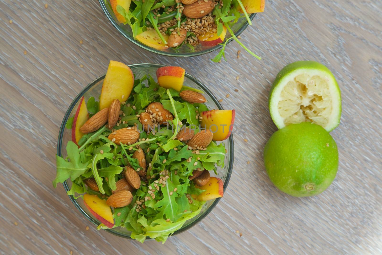 Vitamin salad- rucola with almond, peach and sesame seeds in glass dish. Squeezed green lemon in the background. Top view