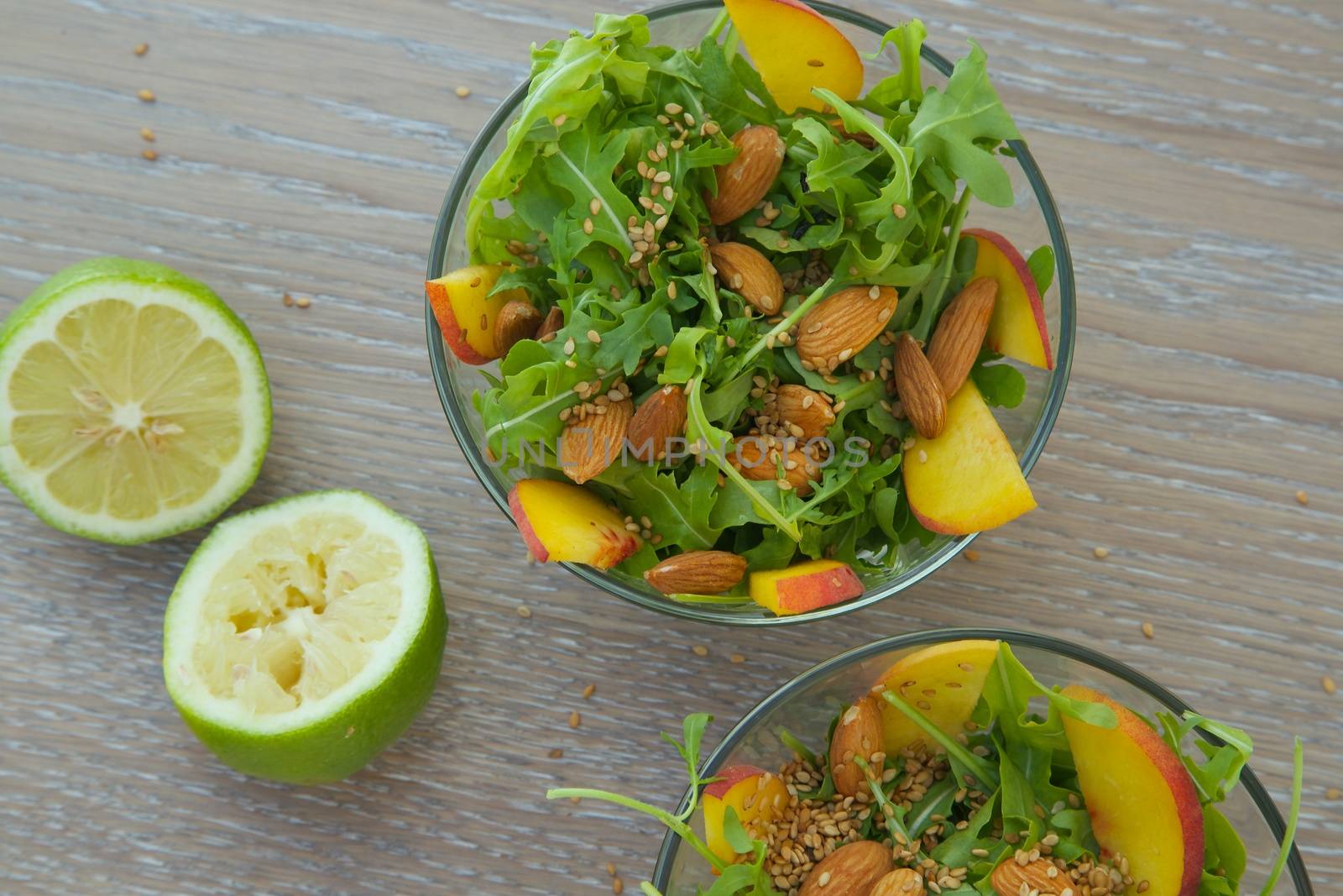 Vitamin salad- rucola with almond, peach and sesame seeds in glass dish. Squeezed lemon in the background. Top view