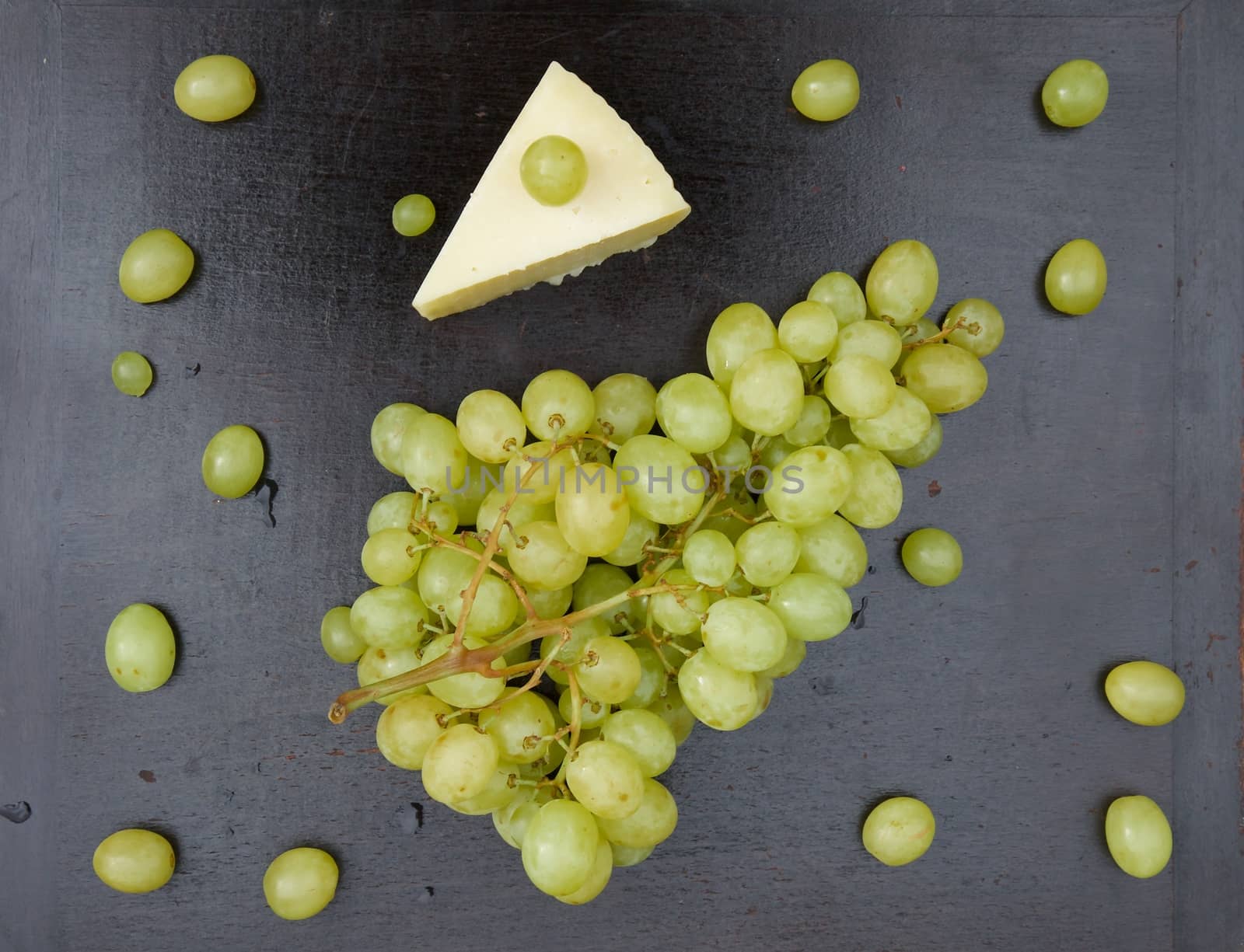 A bunch of white seedless grape and a piece of cheese on the old wooden surface. Top view. Background