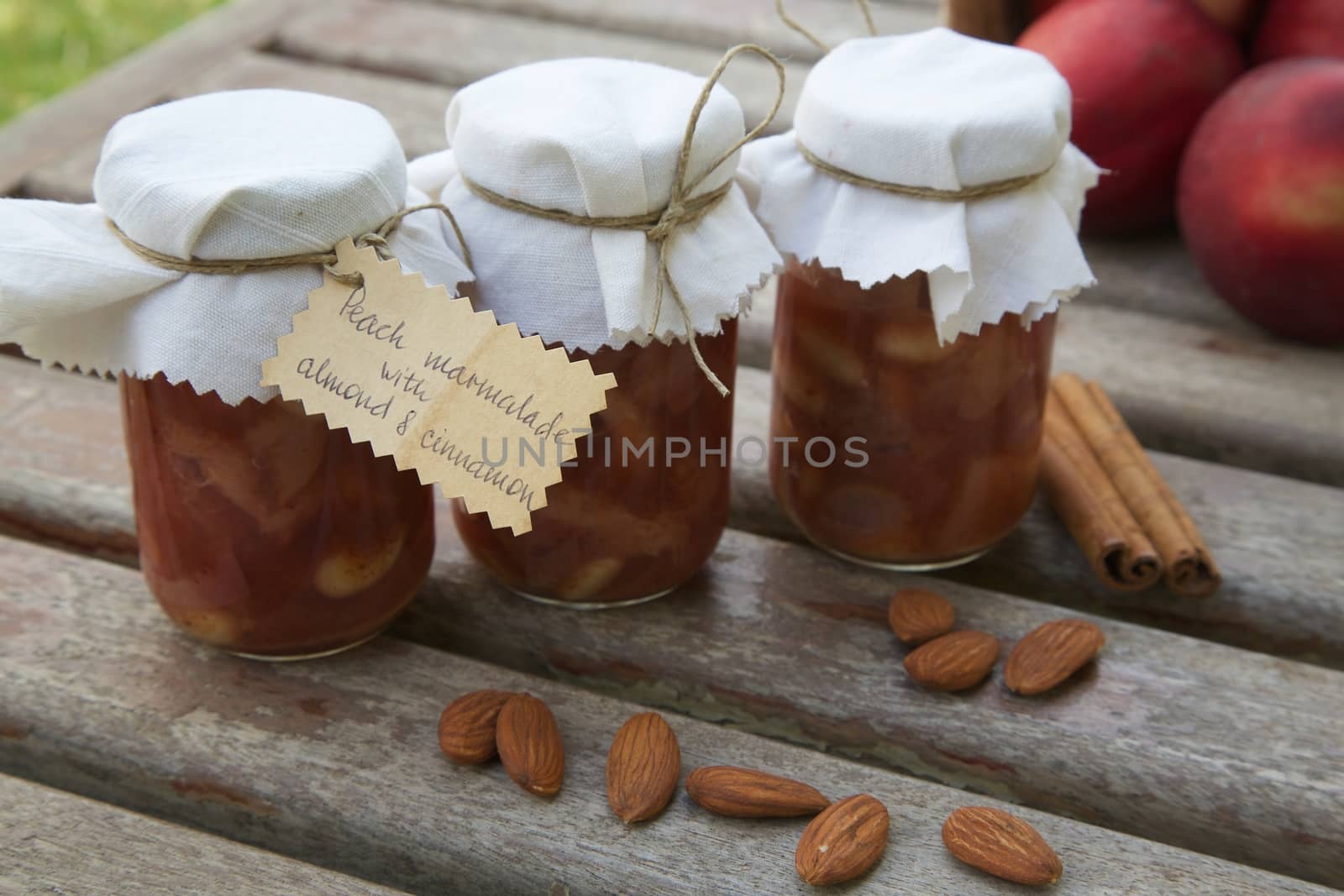 Glasses of homemade peach marmalade with almond nuts and cinnamon on an old wooden surface.Almonds,cinnamon sticks and fresh peaches in the background