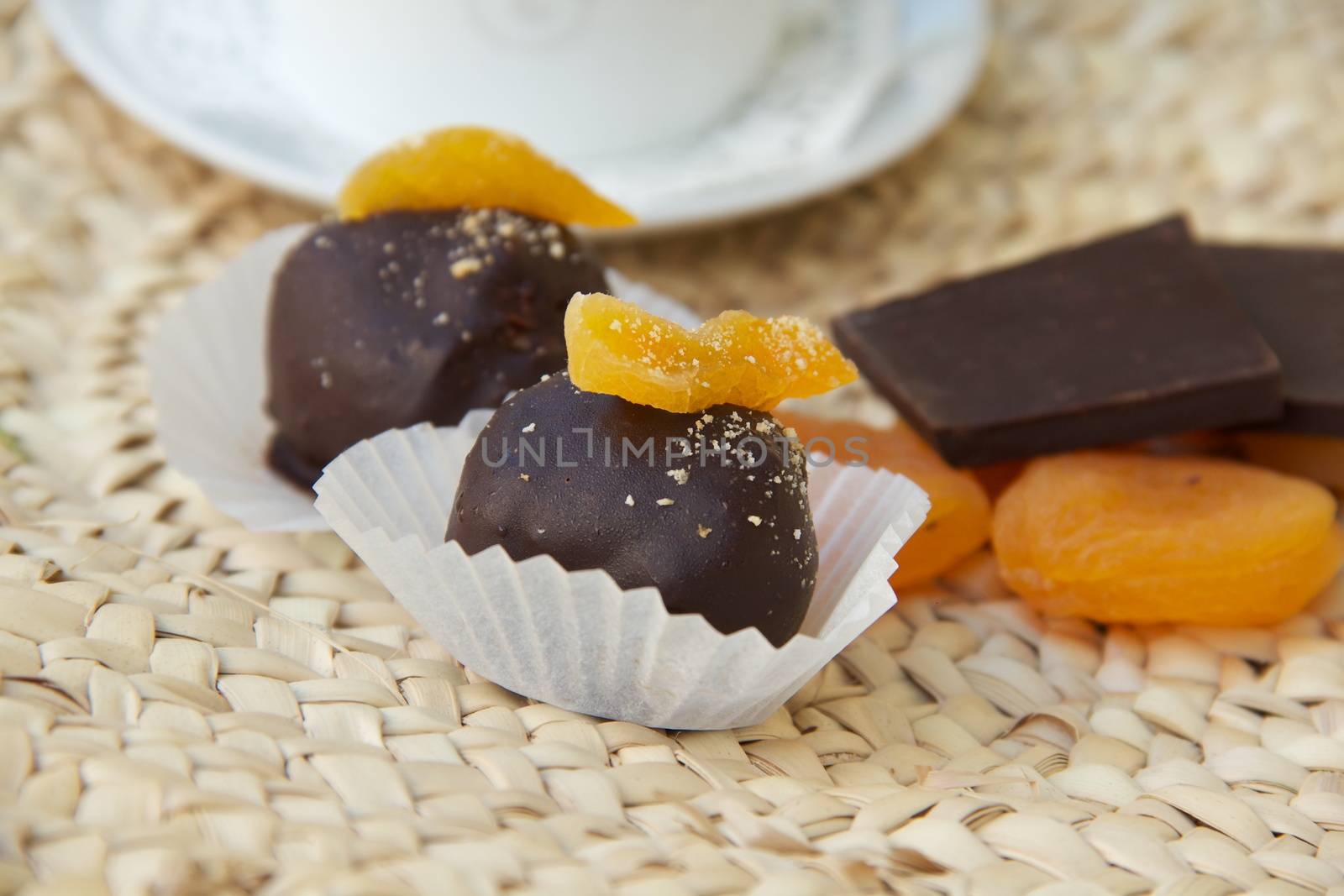 Handmade chocolate truffle with dried apricots on the woven surface. Dried apricots and pieces of black chocolate in the background