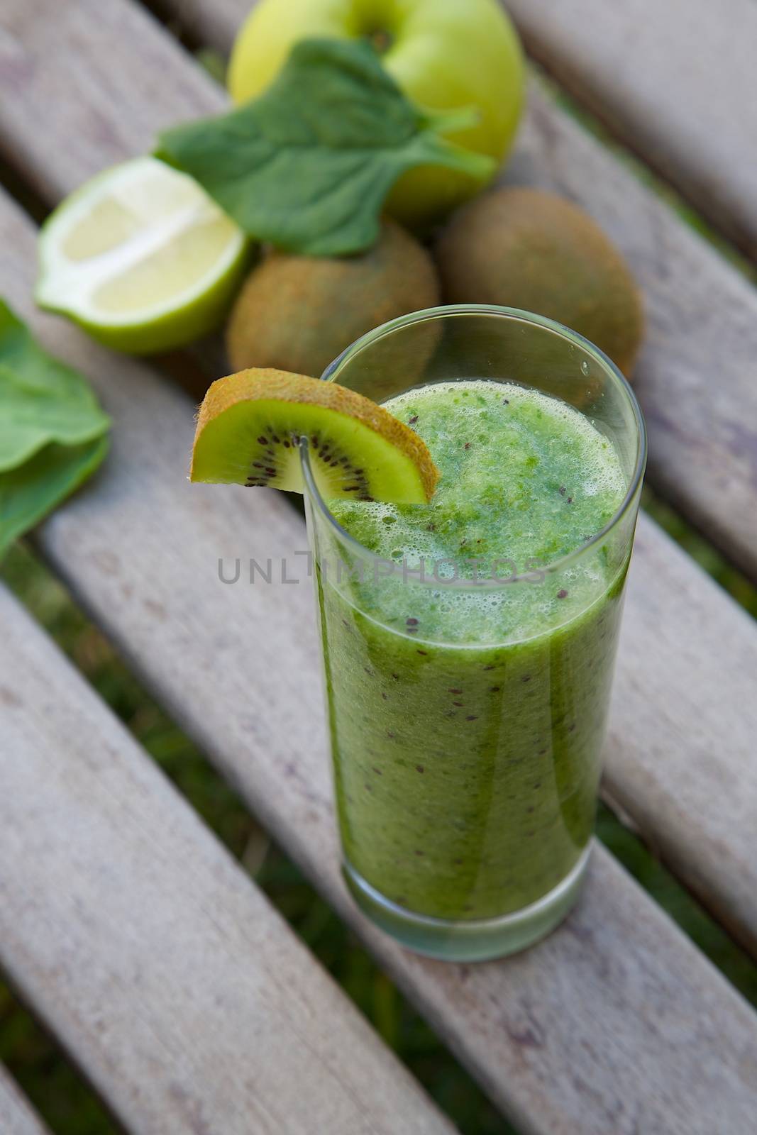 Spinach-kiwi-green apple smoothie in the glass. Kiwi, spinach leaves,green apple and lemon in the background