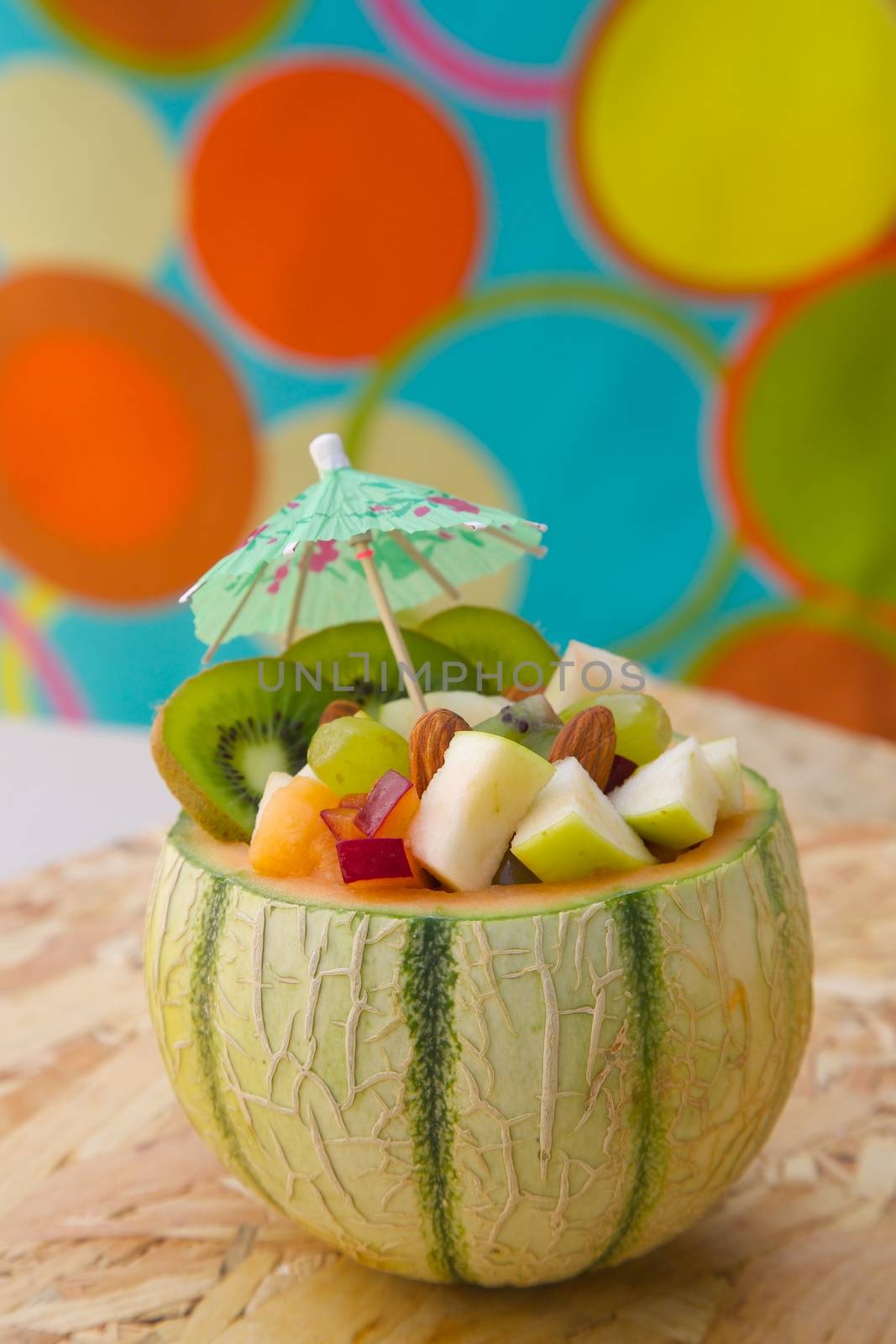 Vitamin dessert- fruit salad in the honeydew melon skin on the wooden surface. Decorated by paper umbrella