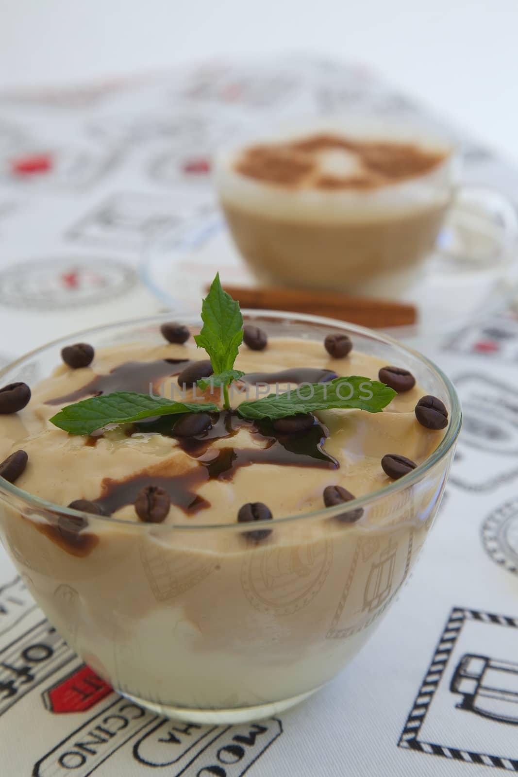 Pudding with cappuccino flavour in a glass dish. Decorated with coffee beans ,chocolate topping and fresh peppermint leaves. A cup of cappuccino in the background