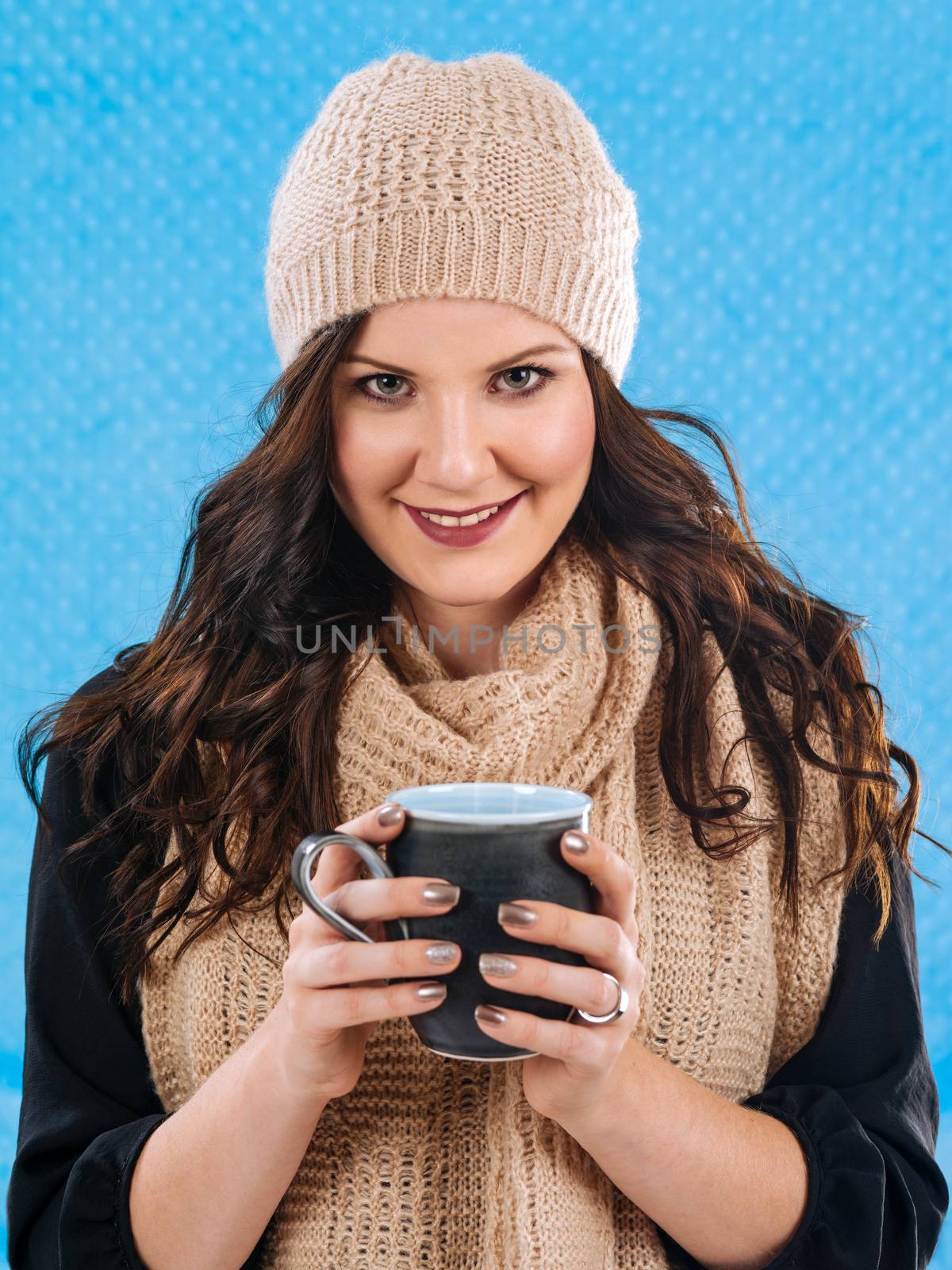 Photo of a beautiful brunette wrapped in warm scarf and hat, drinking a hot coffee, or hot chocolate.