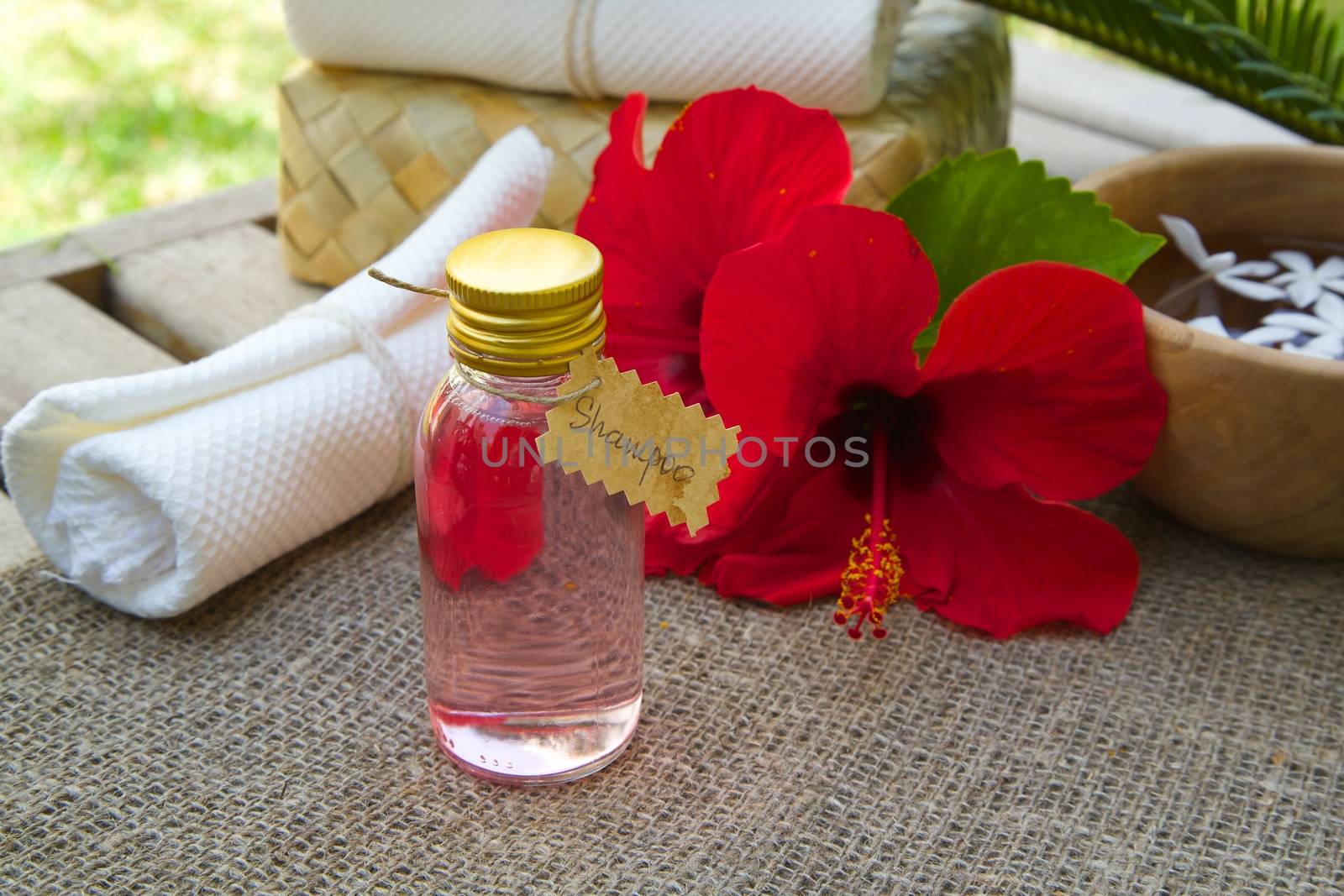 A bottle of hibiscus shampoo. Flowers of hibiscus in the background