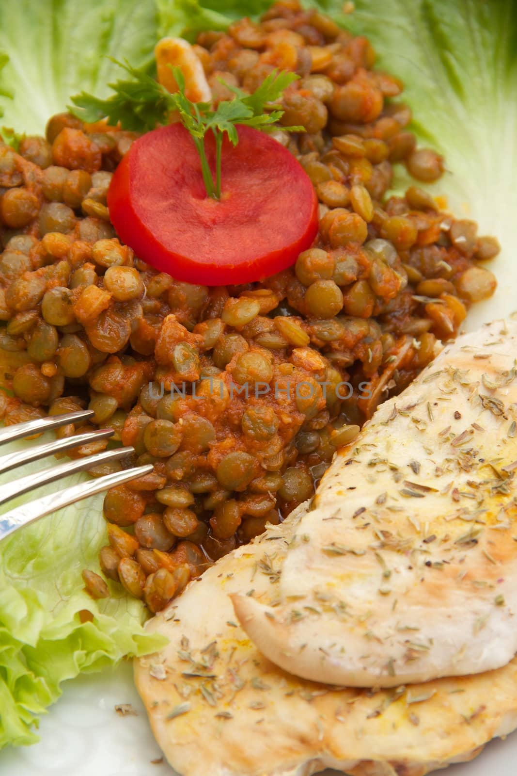 Fitness lunch - stewed green lentils in the tomato sauce with garlic and grilled chicken fillet with oregano. A fork and a knife on the dish. Close up. 