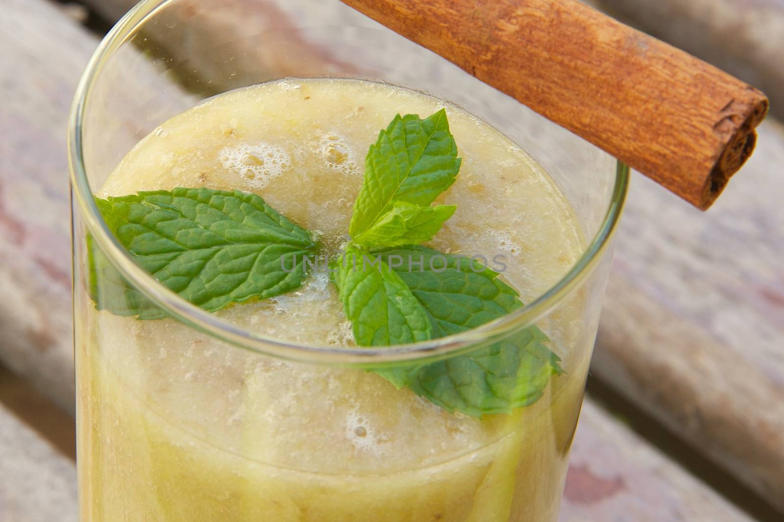 A glass of banana-melon smoothie with fresh peppermint leaves and cinnamon sticks. Close up