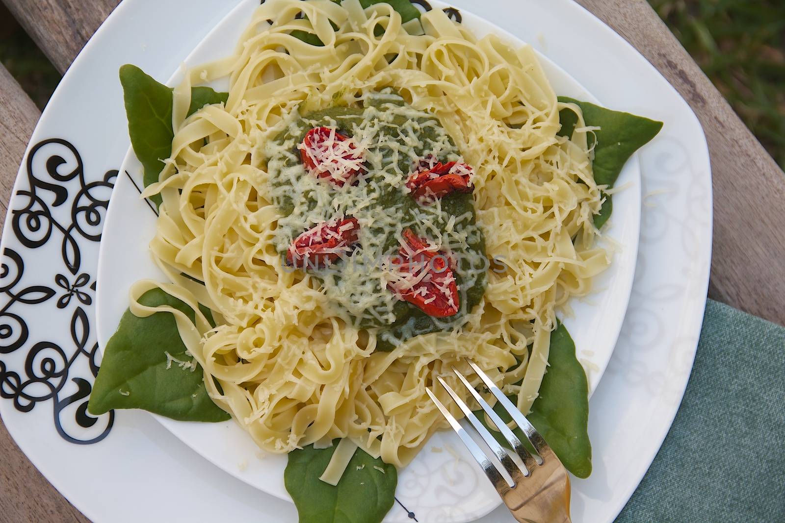 Italian pasta - tagliatelle with spinach, tomatoes and cheese. Fork and green napkin in the background