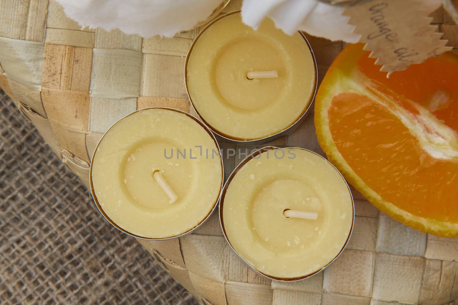 Three candles with orange fragrance and one fourth of an orange. Top view