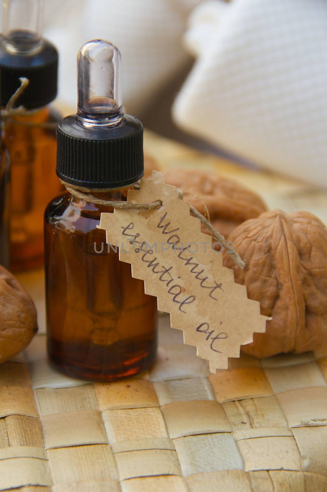 Bottle of walnut essential oil on the woven surface. Walnuts in the background