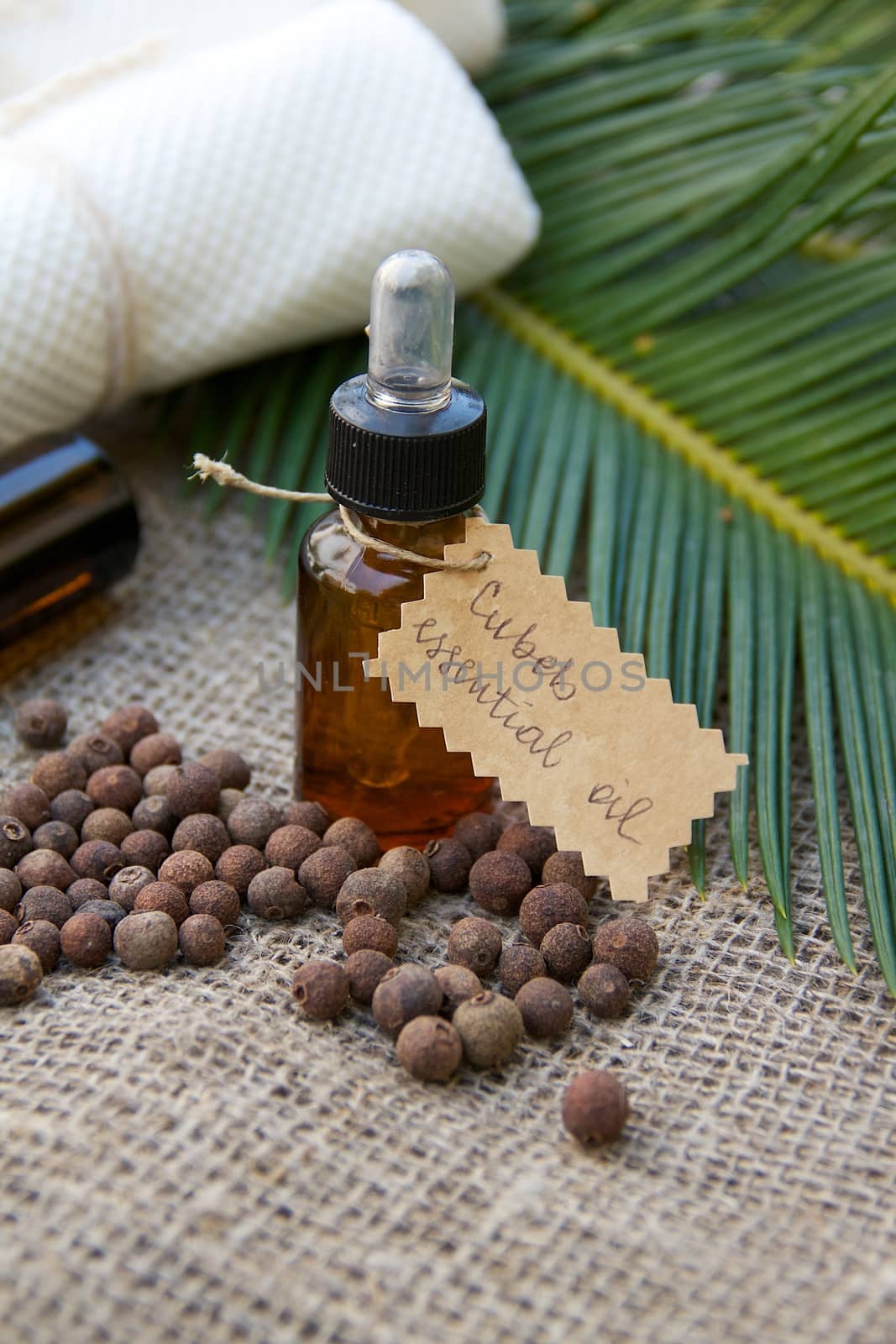 A bottle of cubeb essential oil on the sackcloth. Cubeb berries in the background